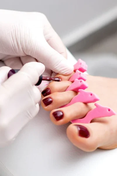 manicure-master-is-painting-female-toenails-with-maroon-nail-polish-by-brush-wearing-white-gloves_141172-4741